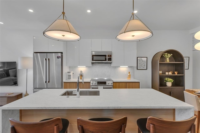 kitchen with a breakfast bar, a sink, white cabinets, appliances with stainless steel finishes, and modern cabinets