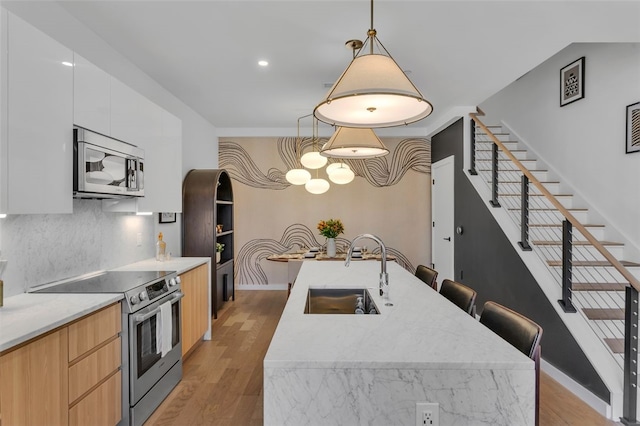 kitchen featuring light wood-type flooring, modern cabinets, a sink, backsplash, and appliances with stainless steel finishes