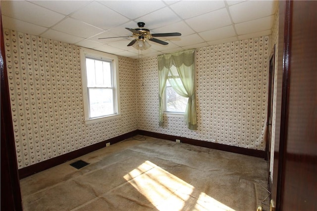 carpeted empty room featuring baseboards, visible vents, wallpapered walls, a drop ceiling, and ceiling fan