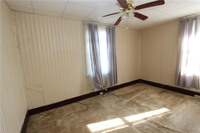 empty room featuring a drop ceiling, baseboards, carpet, and a ceiling fan