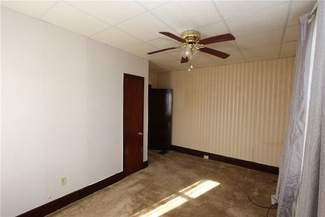 empty room featuring a drop ceiling, baseboards, a ceiling fan, and carpet floors