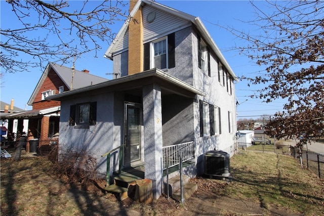 view of side of home with stucco siding, entry steps, fence, cooling unit, and a chimney