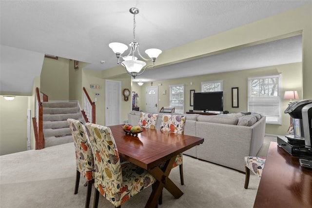 dining space with light colored carpet, a notable chandelier, and stairs