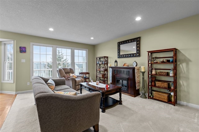 living room featuring a textured ceiling, baseboards, recessed lighting, light carpet, and a glass covered fireplace