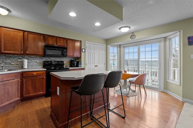 kitchen with a kitchen bar, black appliances, light wood finished floors, decorative backsplash, and light countertops