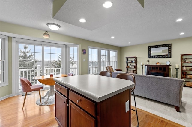 kitchen featuring a breakfast bar, a kitchen island, recessed lighting, a fireplace, and light wood finished floors