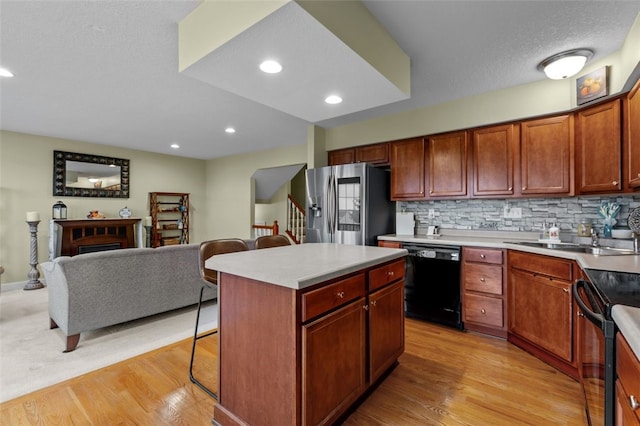 kitchen featuring open floor plan, a kitchen breakfast bar, black appliances, and light wood-style floors