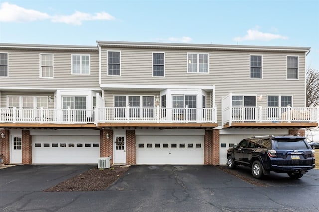 view of property with central air condition unit, a garage, brick siding, and driveway