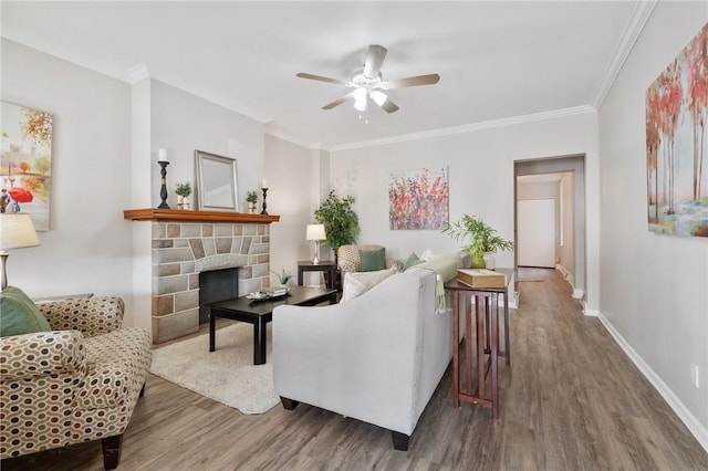 living room featuring wood finished floors, a ceiling fan, baseboards, a fireplace, and ornamental molding