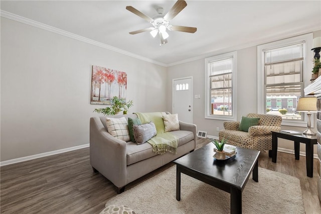 living area featuring wood finished floors, visible vents, baseboards, ceiling fan, and crown molding