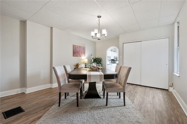 dining space with a drop ceiling, visible vents, wood finished floors, and a chandelier