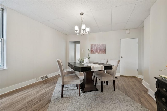 dining space with visible vents, a paneled ceiling, a notable chandelier, and wood finished floors