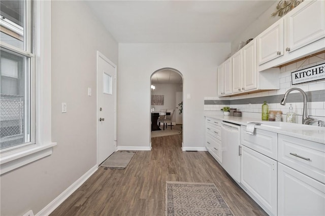 kitchen with dark wood-style floors, white cabinetry, arched walkways, a sink, and dishwasher