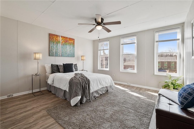 bedroom with ceiling fan, baseboards, wood finished floors, and a decorative wall