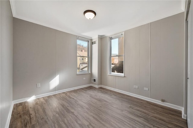 empty room featuring wood finished floors, visible vents, and baseboards