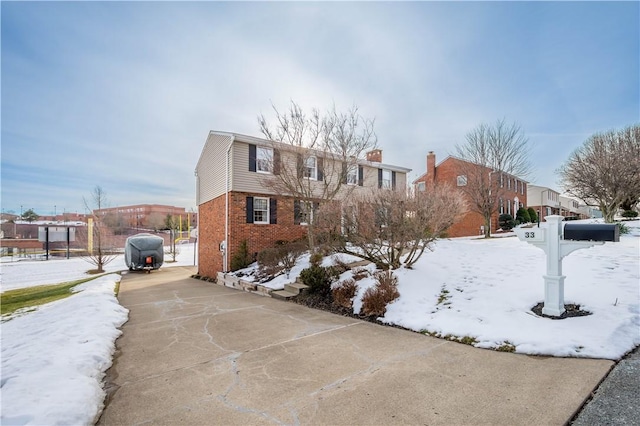 view of front of property with fence, driveway, brick siding, a chimney, and a residential view