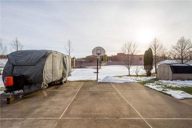 yard layered in snow featuring basketball court, a shed, an outdoor structure, and fence