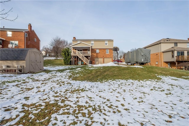 snow covered rear of property featuring a storage shed, an outdoor structure, and stairs