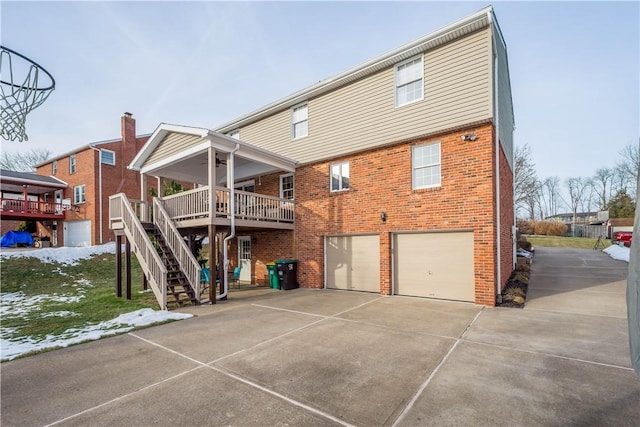 back of property featuring stairway, driveway, brick siding, and an attached garage