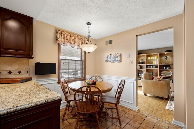 dining space with a wainscoted wall, visible vents, and a textured ceiling