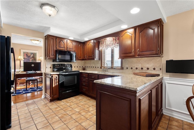 kitchen with a peninsula, a sink, black appliances, a textured ceiling, and backsplash