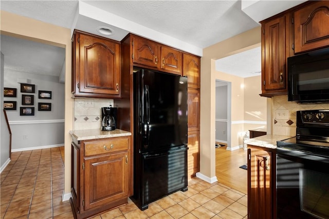 kitchen with light tile patterned floors, decorative backsplash, black appliances, and baseboards