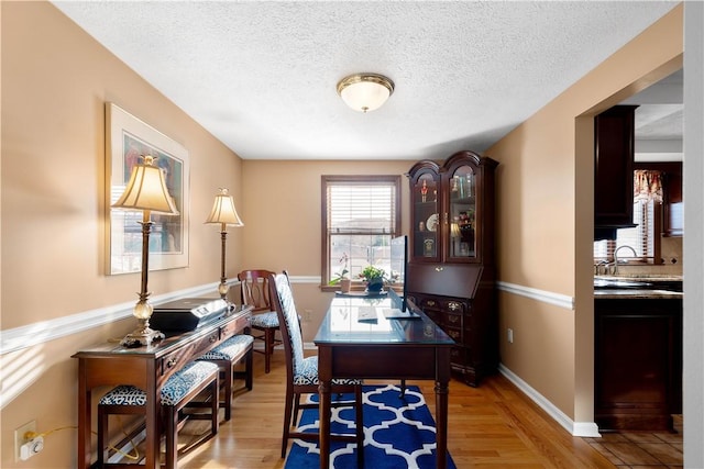 dining space with a textured ceiling, light wood-type flooring, and baseboards