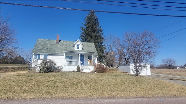 new england style home with covered porch, a chimney, and a front yard