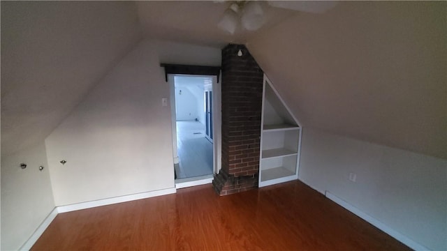 bonus room featuring built in shelves, lofted ceiling, a ceiling fan, wood finished floors, and baseboards