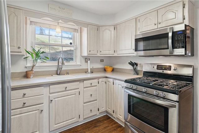 kitchen with appliances with stainless steel finishes, light countertops, dark wood-type flooring, and a sink