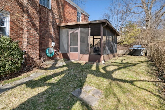 back of property with brick siding, a lawn, and a sunroom