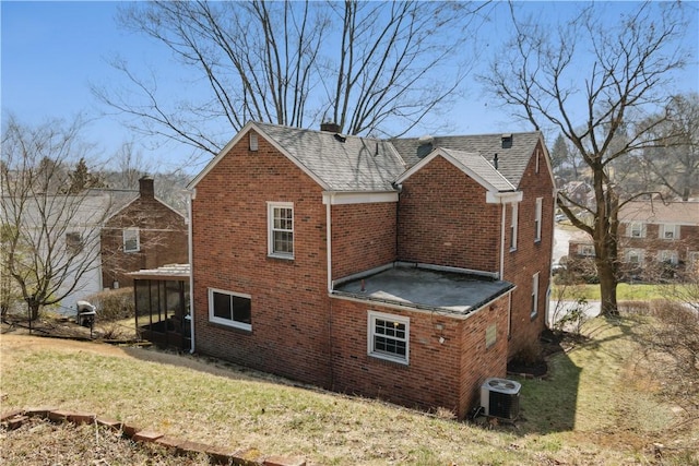 view of home's exterior with brick siding, central air condition unit, roof with shingles, a lawn, and a sunroom