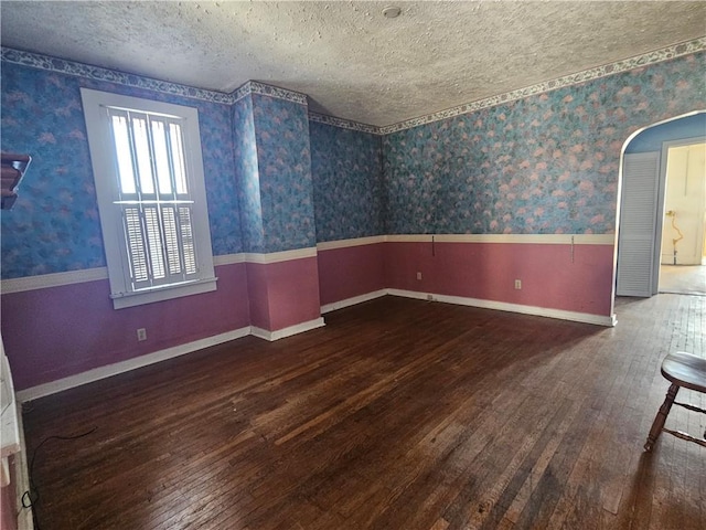 unfurnished room featuring a wainscoted wall, a textured ceiling, hardwood / wood-style floors, arched walkways, and wallpapered walls