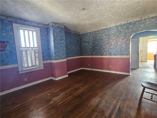 unfurnished room with a wainscoted wall, a textured ceiling, wood finished floors, arched walkways, and wallpapered walls