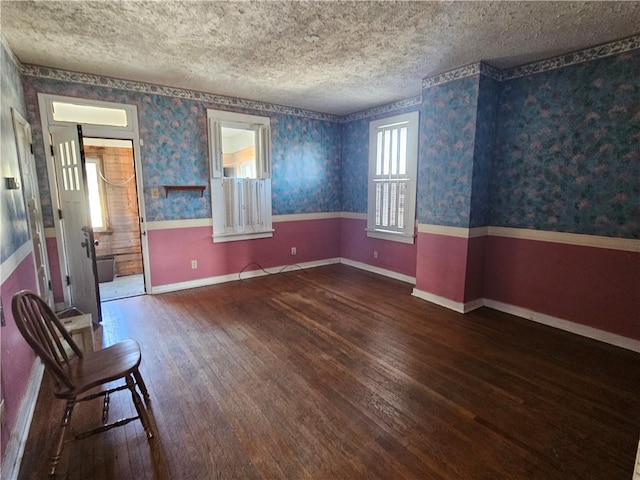 empty room featuring baseboards, wallpapered walls, wainscoting, wood-type flooring, and a textured ceiling