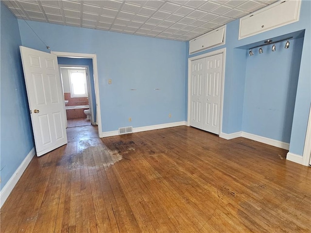 unfurnished bedroom featuring hardwood / wood-style floors, baseboards, visible vents, and an ornate ceiling