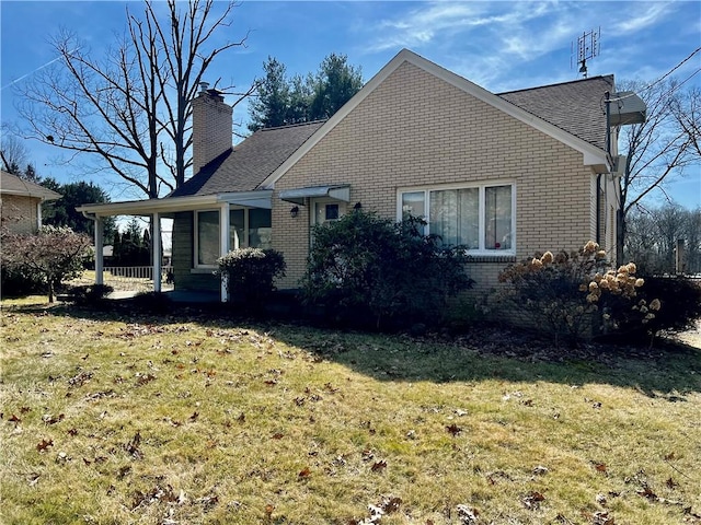 rear view of house featuring brick siding, a lawn, and a chimney