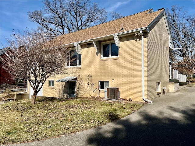 rear view of house featuring central AC unit, brick siding, and roof with shingles