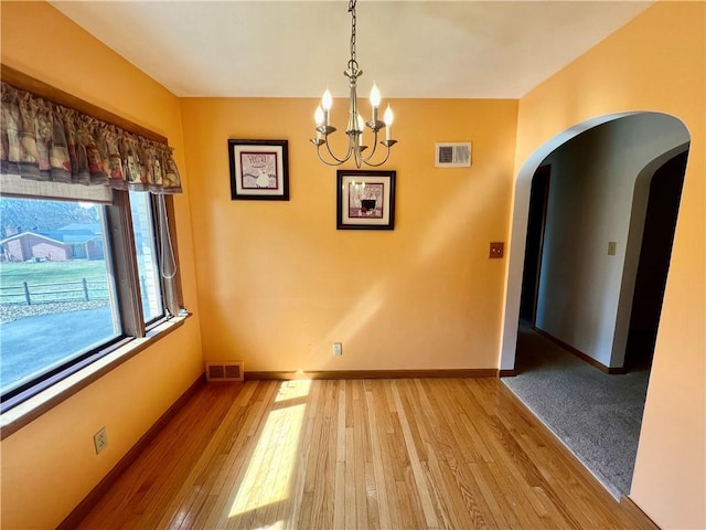 unfurnished dining area with an inviting chandelier, arched walkways, visible vents, and light wood finished floors