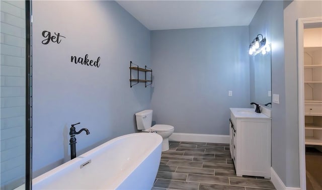 bathroom with wood finish floors, toilet, baseboards, a soaking tub, and vanity