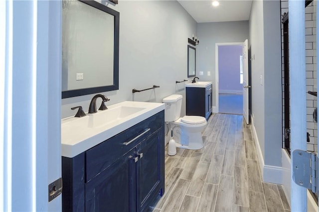 full bath featuring a sink, wood finish floors, toilet, and two vanities