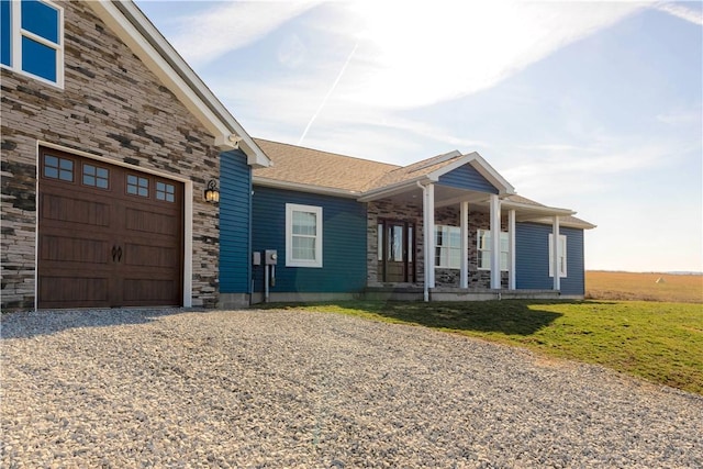 view of front of house featuring roof with shingles, gravel driveway, an attached garage, covered porch, and stone siding