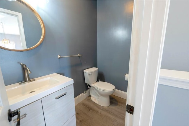 half bath with baseboards, toilet, wood finished floors, and vanity