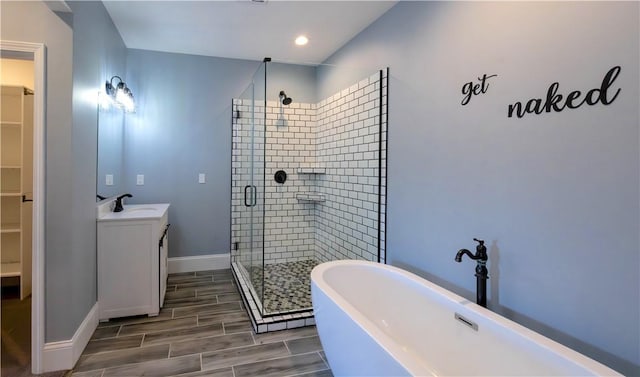 full bath featuring a shower stall, a walk in closet, baseboards, wood tiled floor, and a freestanding tub