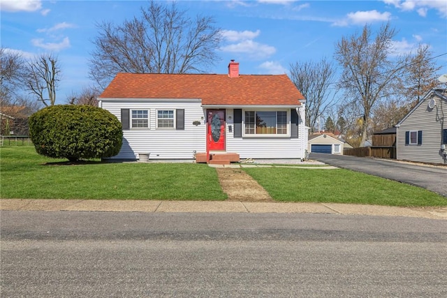 view of front of home with an outdoor structure, a front yard, a detached garage, and a chimney