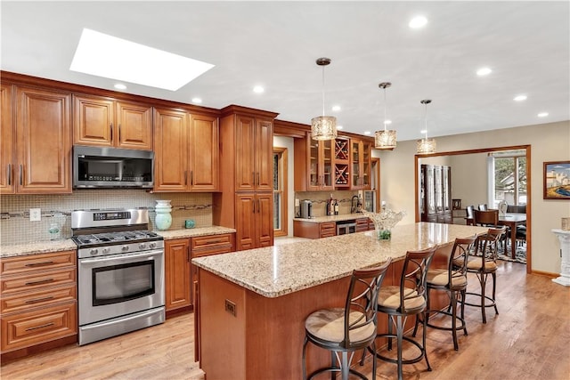 kitchen featuring light stone counters, stainless steel appliances, brown cabinets, and a breakfast bar area