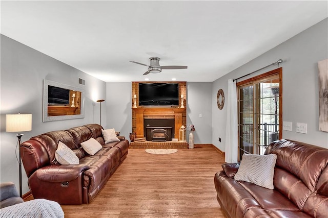 living room featuring visible vents, light wood-style flooring, a fireplace, baseboards, and ceiling fan