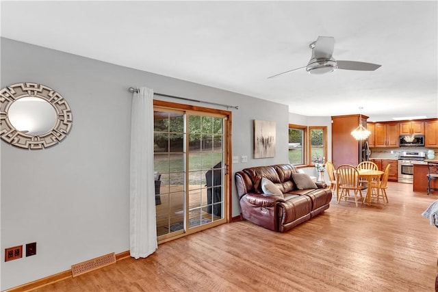 living room with baseboards, ceiling fan with notable chandelier, visible vents, and light wood-type flooring