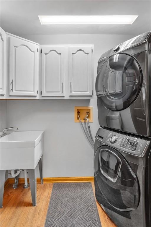 laundry area with cabinet space, wood finished floors, baseboards, and stacked washer and dryer