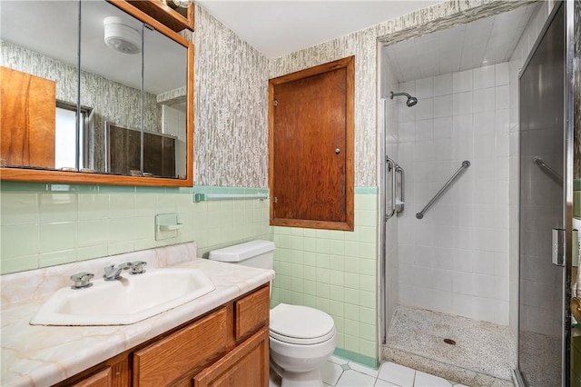 bathroom with a shower stall, wallpapered walls, toilet, wainscoting, and tile walls